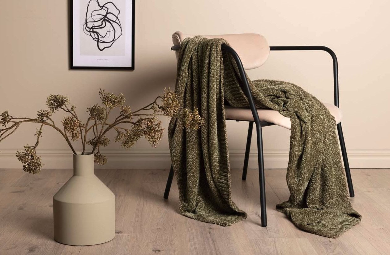 Mysig fåtölj med filt och konstnärlig växt i elegant hem.